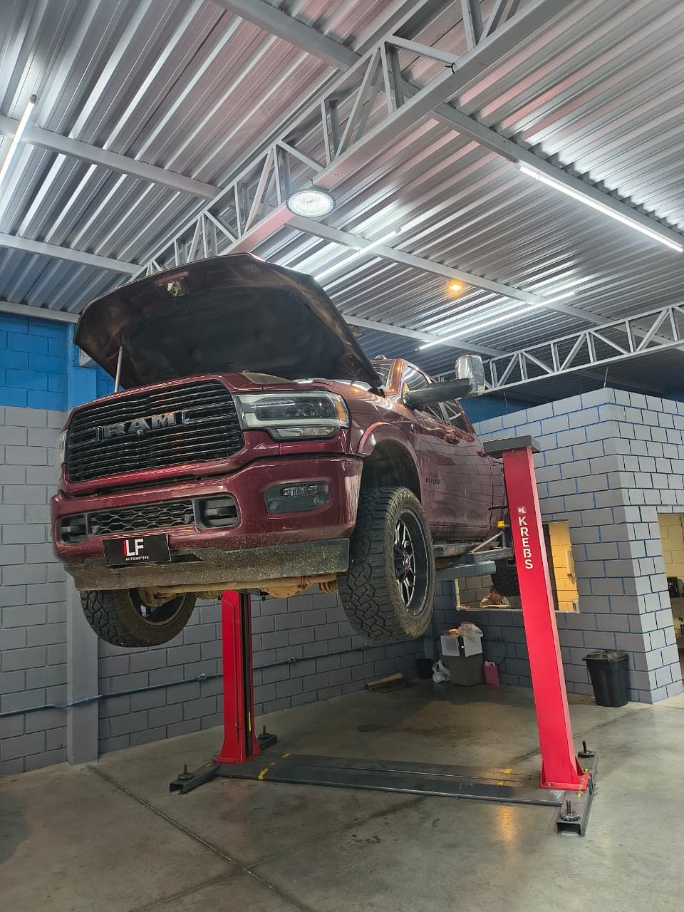 Ram 2500 vermelha suspensa no elevador da oficina, com capô aberto